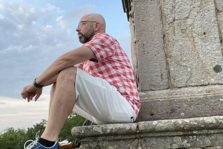 Wanderer sitzt an einem Sommerabend am Sockel des Denkmals auf dem Gipfel der Milseburg