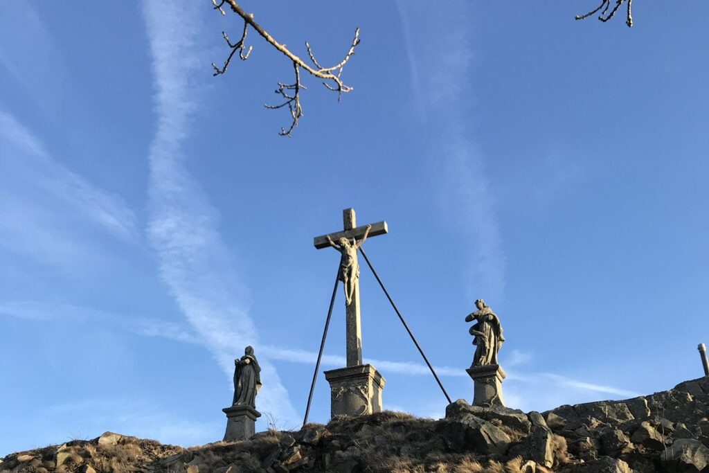 Kreuzigungsgruppe mit Gipfelkreuz und zwei Figuren auf dem Gipfel der Milseburg vor blauem Himmel