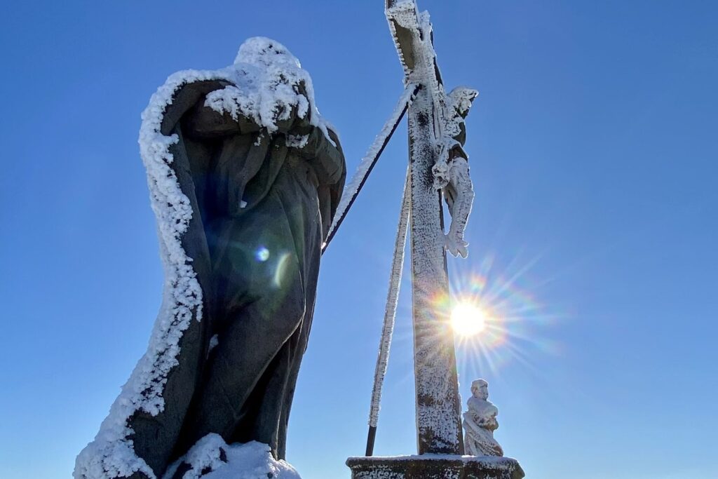 Mit Eis und Schnee überzogene Figur und Gipfelkreuz auf der Milseburg im Winter