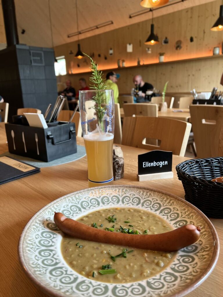 Teller mit Erbsensuppe und Bratwurst auf einem Holztisch in der Milseburghütte HeiMatt