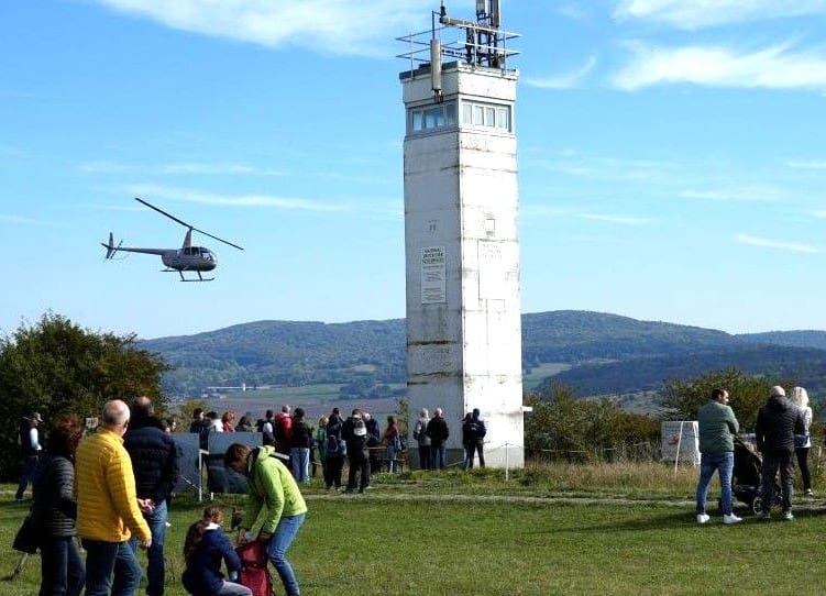 Besucher auf der Wiese vor dem Beobachtungsturm von Point Alpha, im Hintergrund ein Hubschrauber