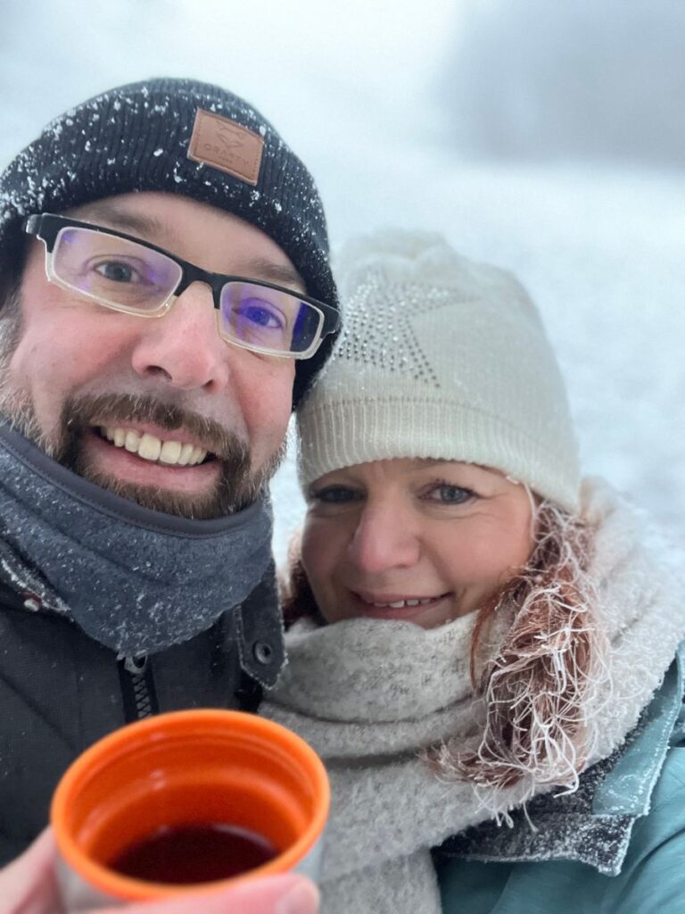 Paar in Wintermützen mit einem Becher Glühwein beim Abstieg im Schnee