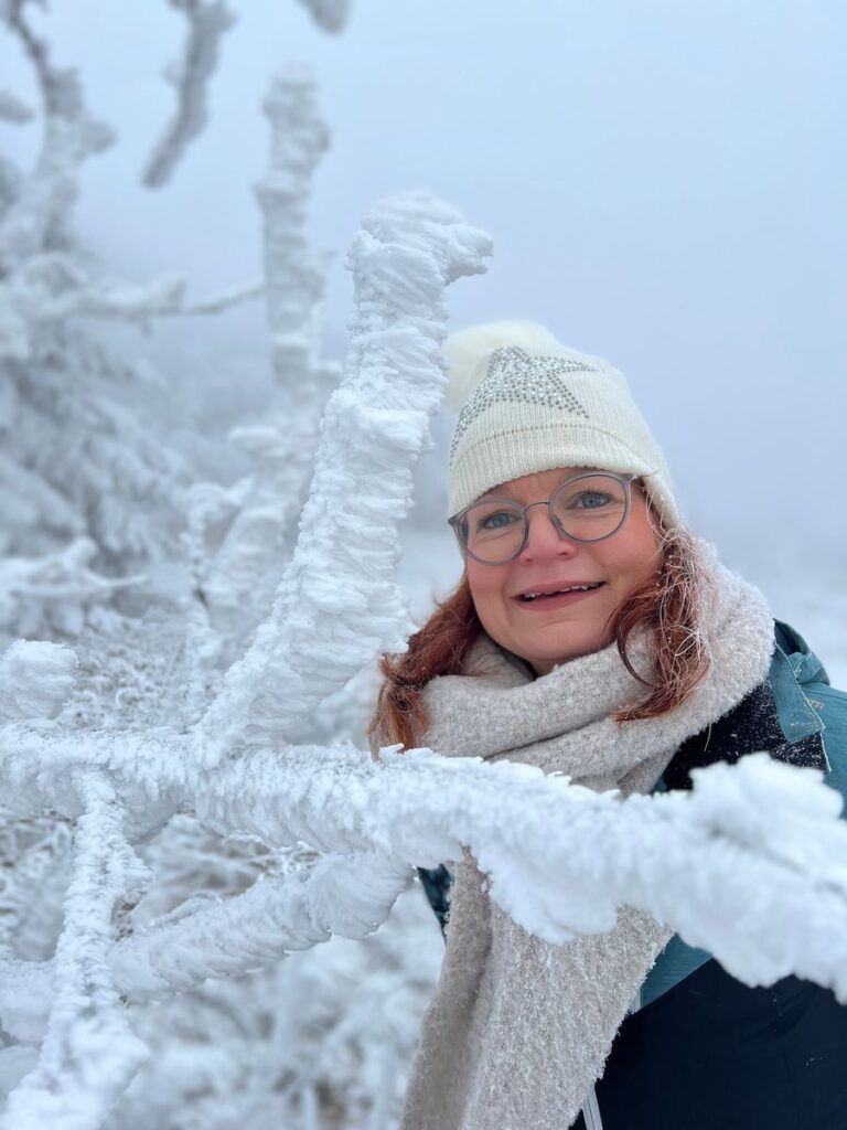 Frau mit Wintermütze und Schal hinter einem dick mit Raureif überzogenen Zweig in der Rhön