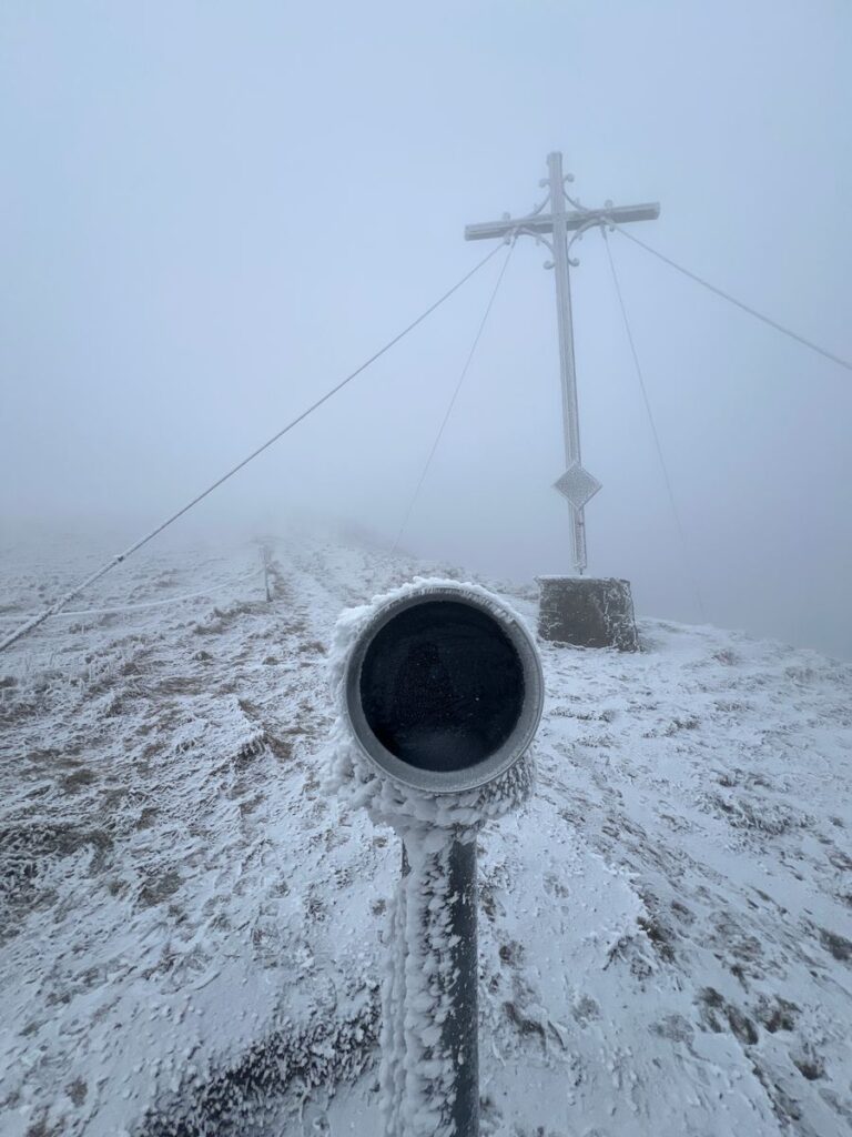 Vereistes Fernrohr vor dem Gipfelkreuz auf dem Pferdskopf im dichten Nebel