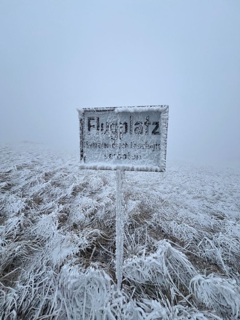 Dick mit Raureif überzogenes Schild Flugplatz im gefrorenen Gras auf der Wasserkuppe