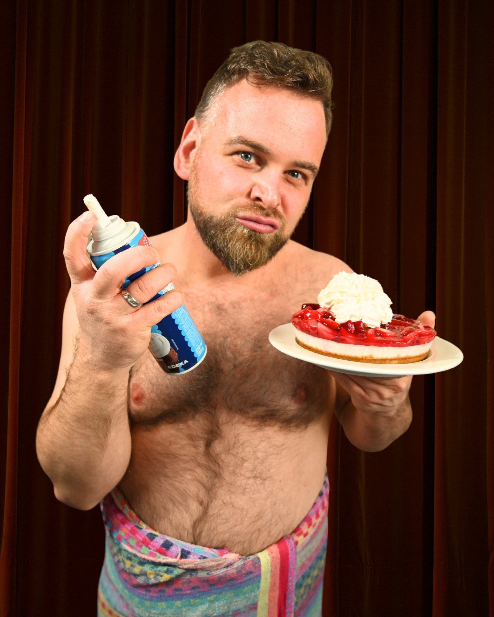 André Haedicke mit Sahnespray und Kirschtorte vor rotem Vorhang