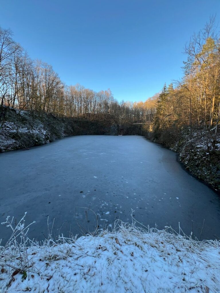 Zugefrorener Basaltsee Ulmenstein im Winter unter blauem Himmel
