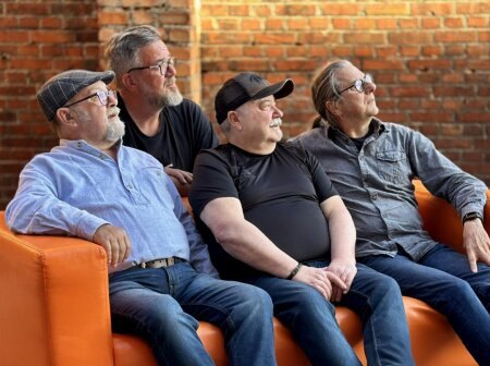 Die vier Musiker von Big Minna auf einem orangefarbenen Sofa vor einer Backsteinwand