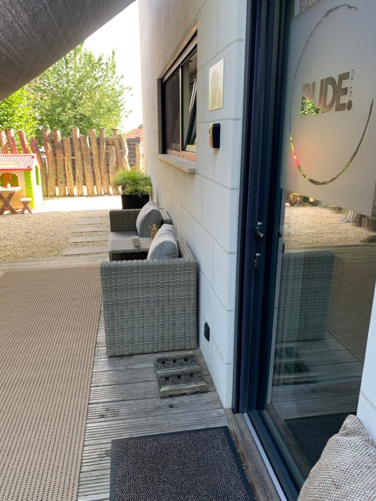 Eingang der BUDE.29 an der Terrasse mit Glastür und Sitzmöbeln