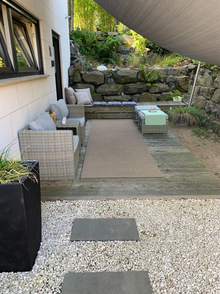Terrasse der BUDE.29 mit Loungemöbeln, Natursteinmauer und Sonnensegel
