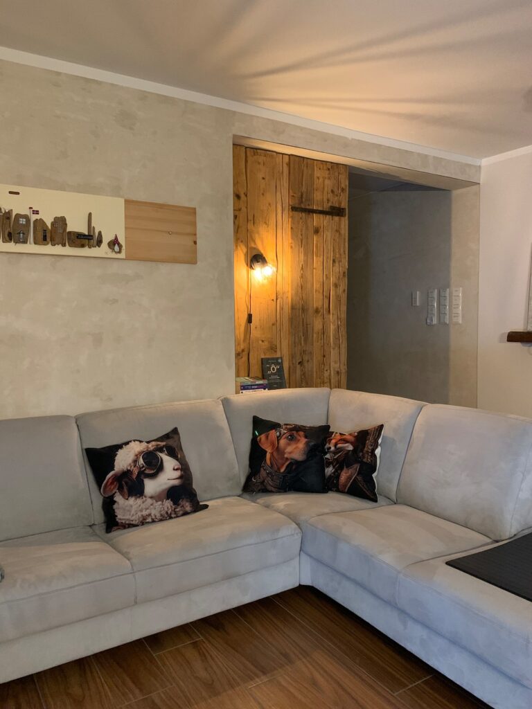 Wohnzimmer der BUDE.29 mit großem grauem Ecksofa und Holzwand