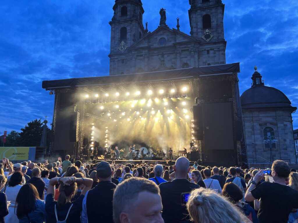 Beleuchtete Bühne bei einem Domplatzkonzert in Fulda, dahinter die Türme des Doms in der Abenddämmerung.