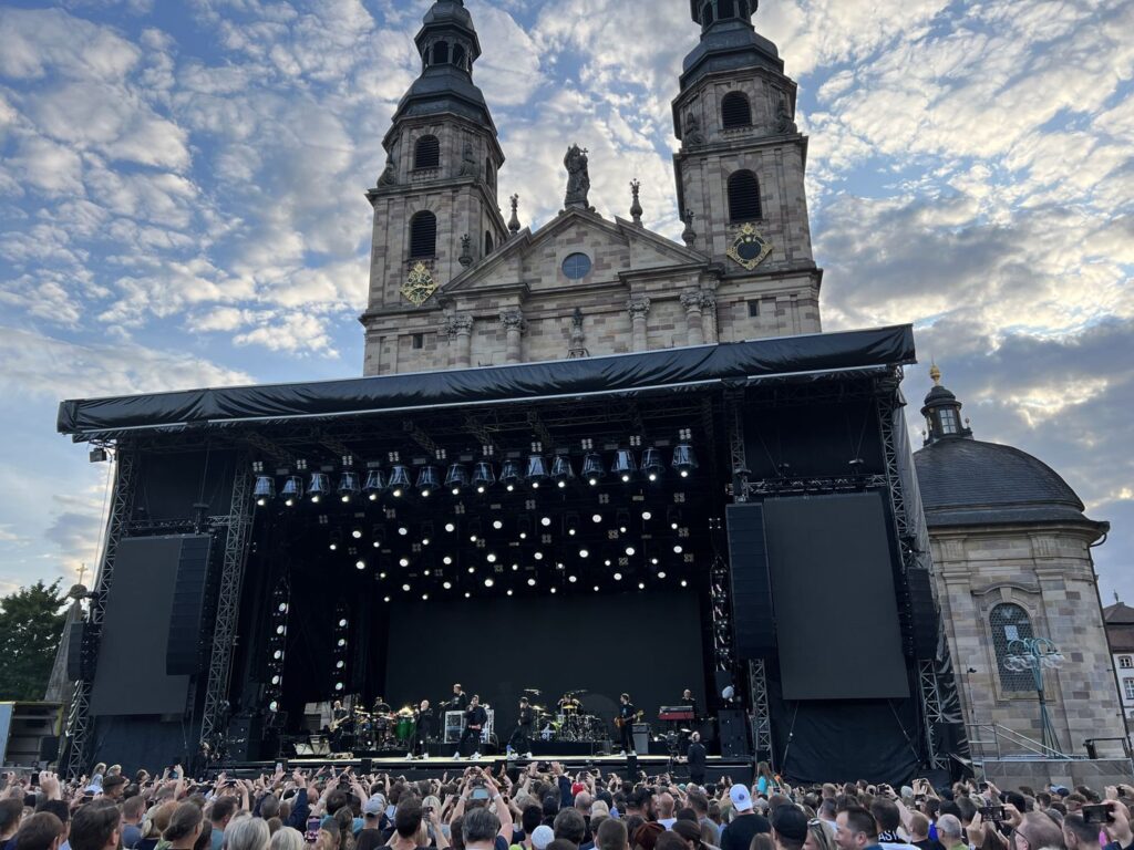 Bühne eines Domplatzkonzerts vor der Barockfassade des Fuldaer Doms, davor viele Besucher.
