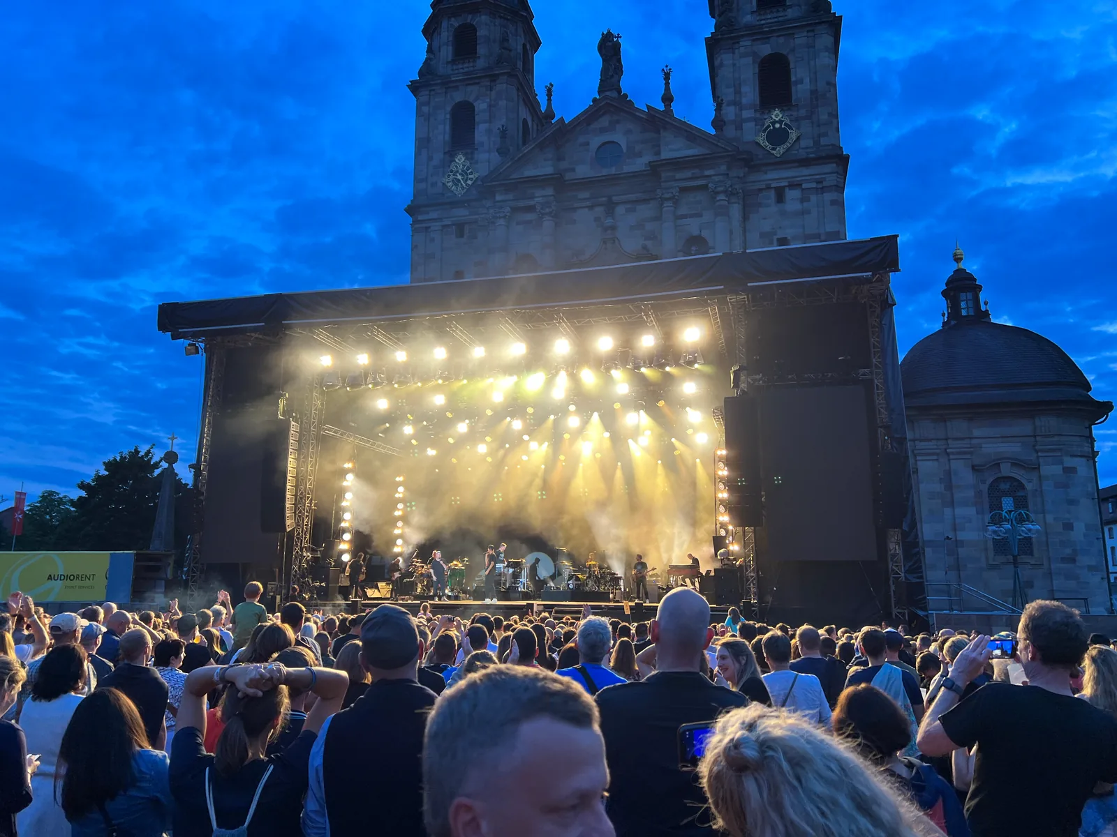 Beleuchtete Konzertbühne vor der Fassade des Fuldaer Doms zur blauen Stunde, davor das Publikum auf dem Domplatz