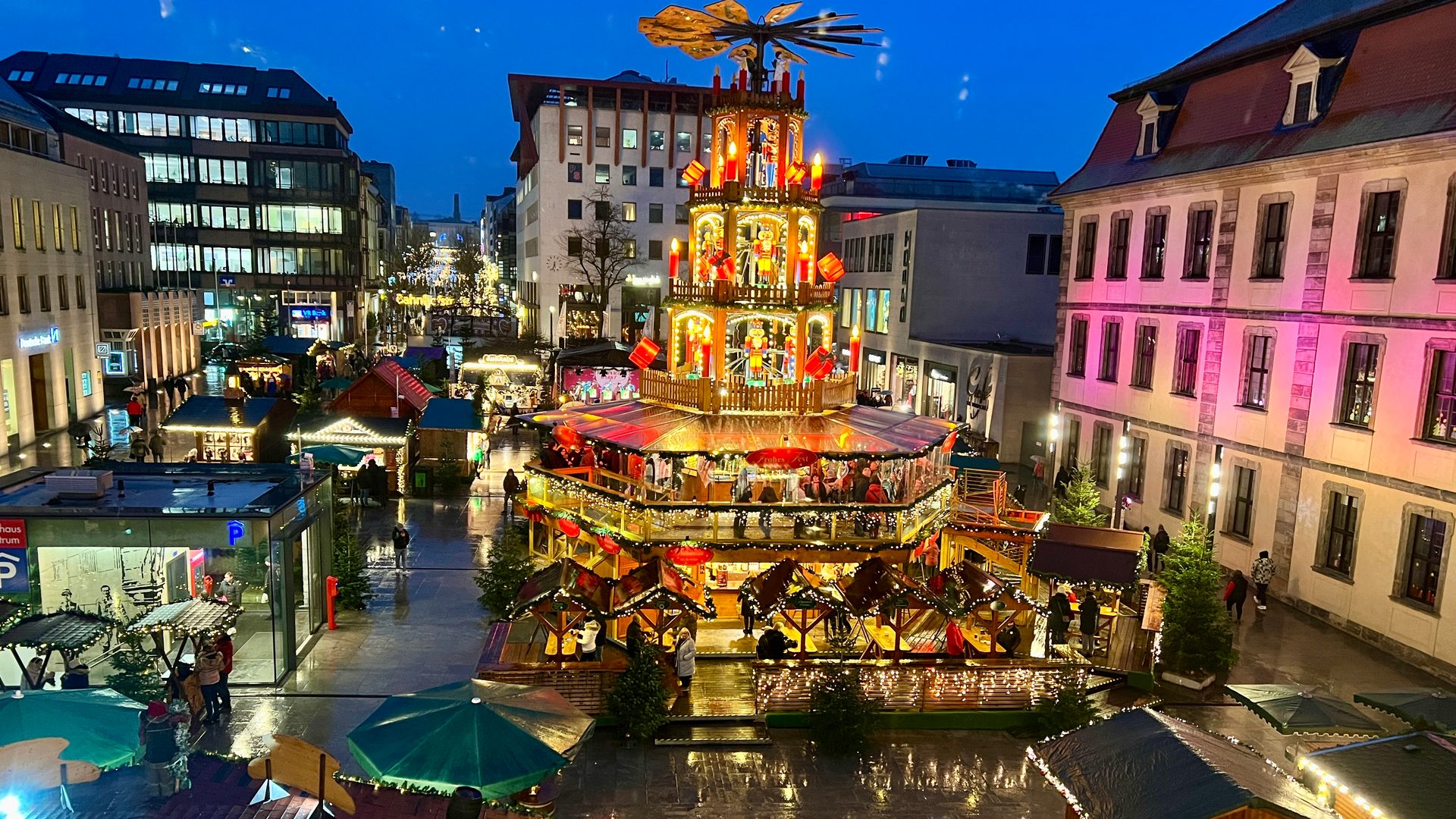 Blick von oben auf die beleuchtete Weihnachtspyramide und die Buden des Fuldaer Weihnachtsmarkts am Universitätsplatz zur blauen Stunde