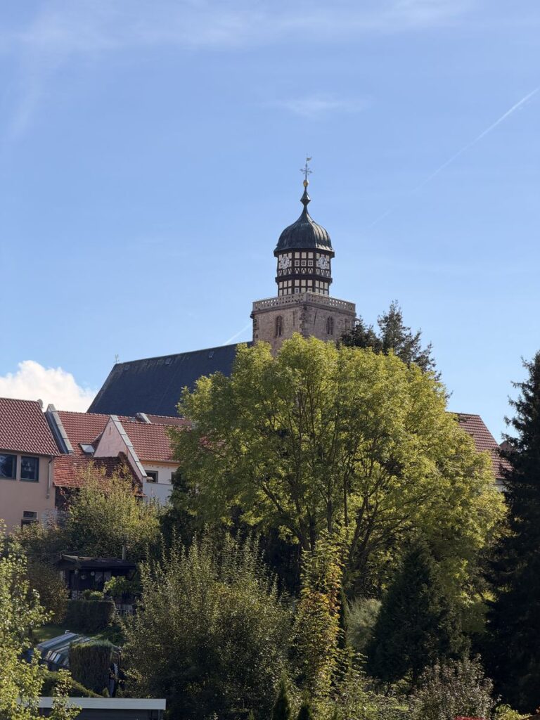 Turm der Stadtkirche Geisa mit Fachwerkaufsatz über herbstlichen Bäumen bei blauem Himmel