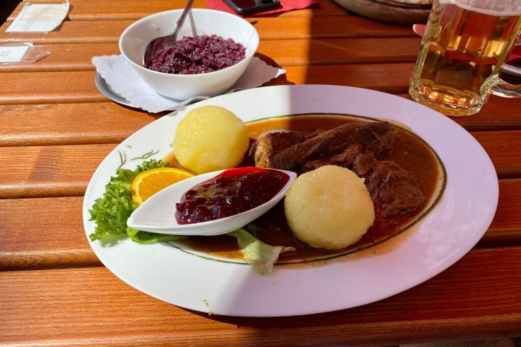 Braten mit Klößen, Rotkraut und Preiselbeeren auf der Terrasse des Holzberghofs