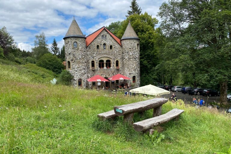 Jagdschloss Holzberghof mit Türmchen und Biergarten, davor eine Holzbank auf der Wiese