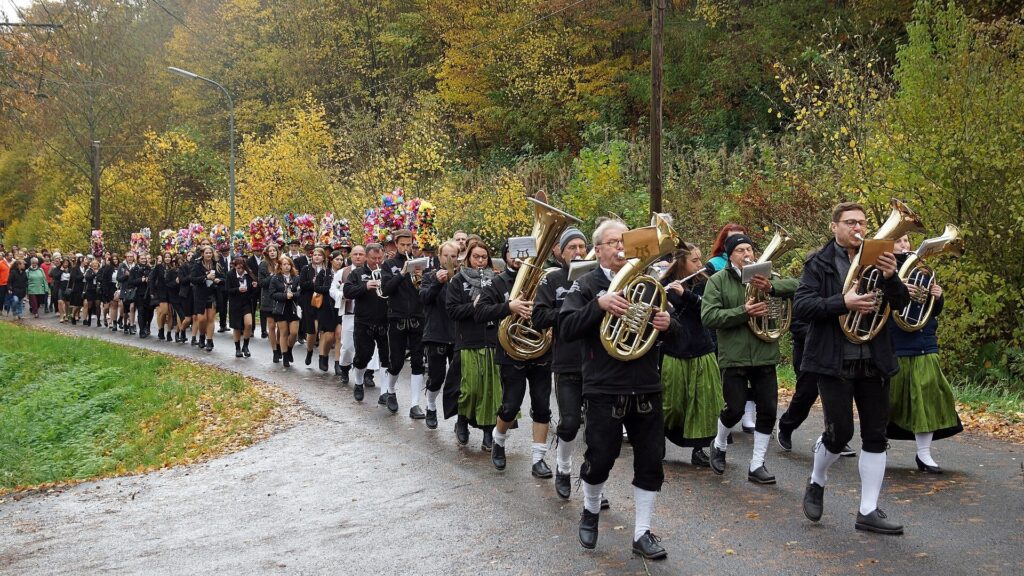 Kirmeszug mit Blaskapelle und Kirmespaaren auf einer herbstlichen Dorfstraße in Hettenhausen in der Rhön
