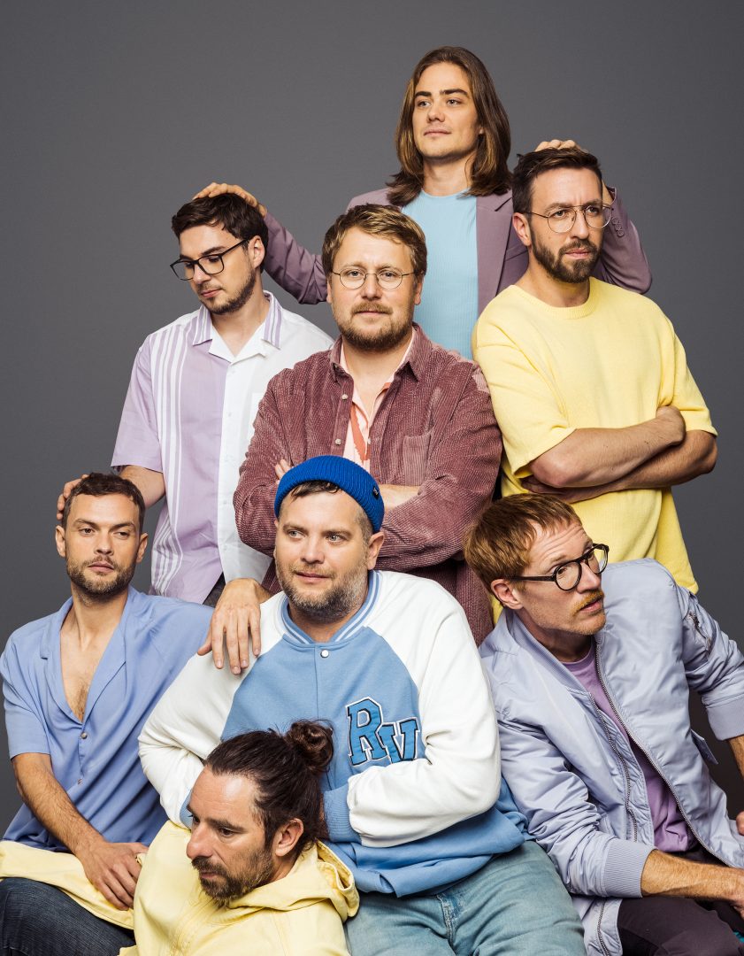 Die Musiker von LaBrassBanda mit Blechblasinstrumenten vor buntem Hintergrund
