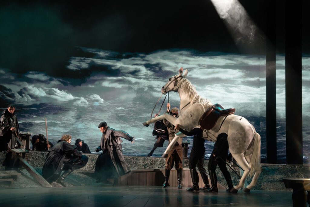 Szene aus dem Musical Der Schimmelreiter: Das Ensemble mit dem sich aufbäumenden Schimmel vor Wolkenkulisse.