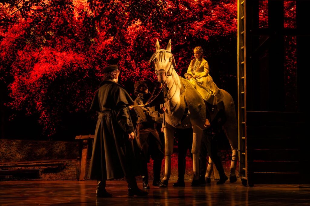 Szene aus dem Musical Der Schimmelreiter: Reiterin auf dem Schimmel unter einem rot leuchtenden Baum.