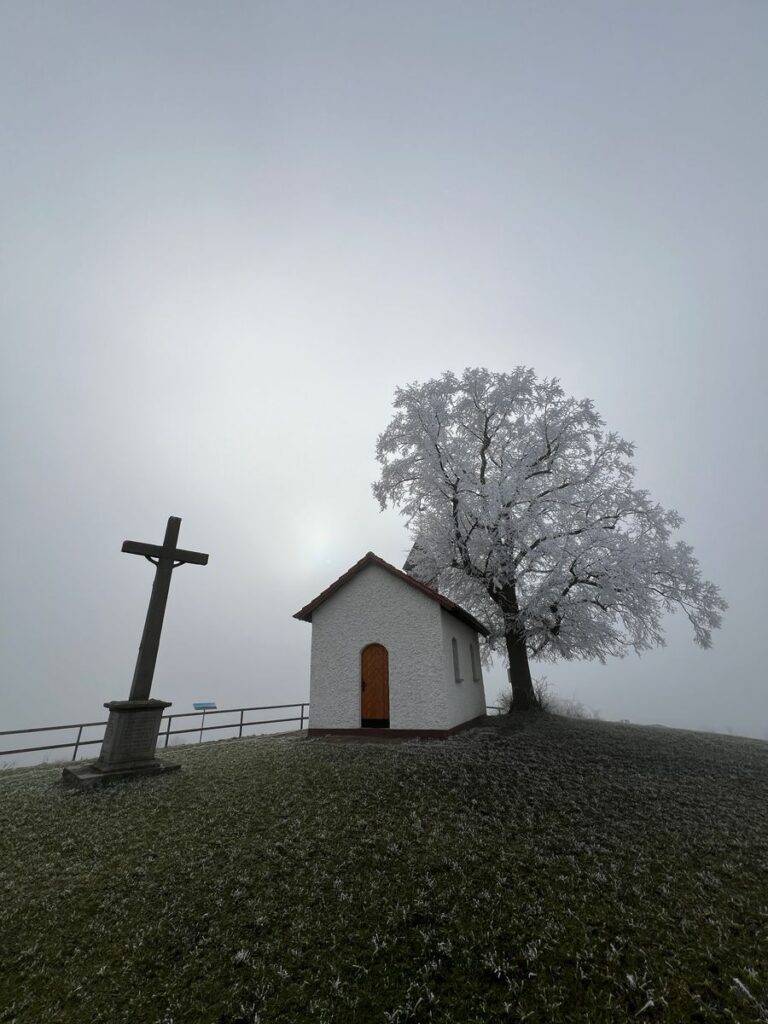 Kleine weiße Kapelle bei Hofaschenbach mit Steinkreuz und raureifbedecktem Baum im Nebel