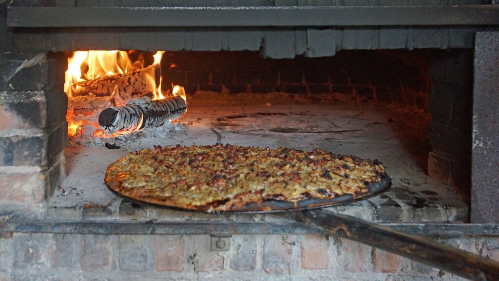 Ein runder Ploatz liegt im brennenden Holzbackofen im Rhöner Museumsdorf Tann