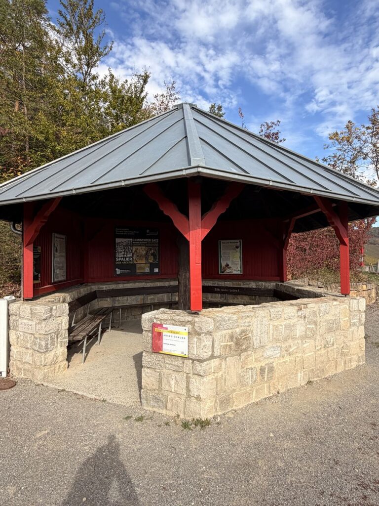 Offener Pavillon mit rotem Holzgebälk und Natursteinmauer am Aussichtspunkt in den Weinbergen