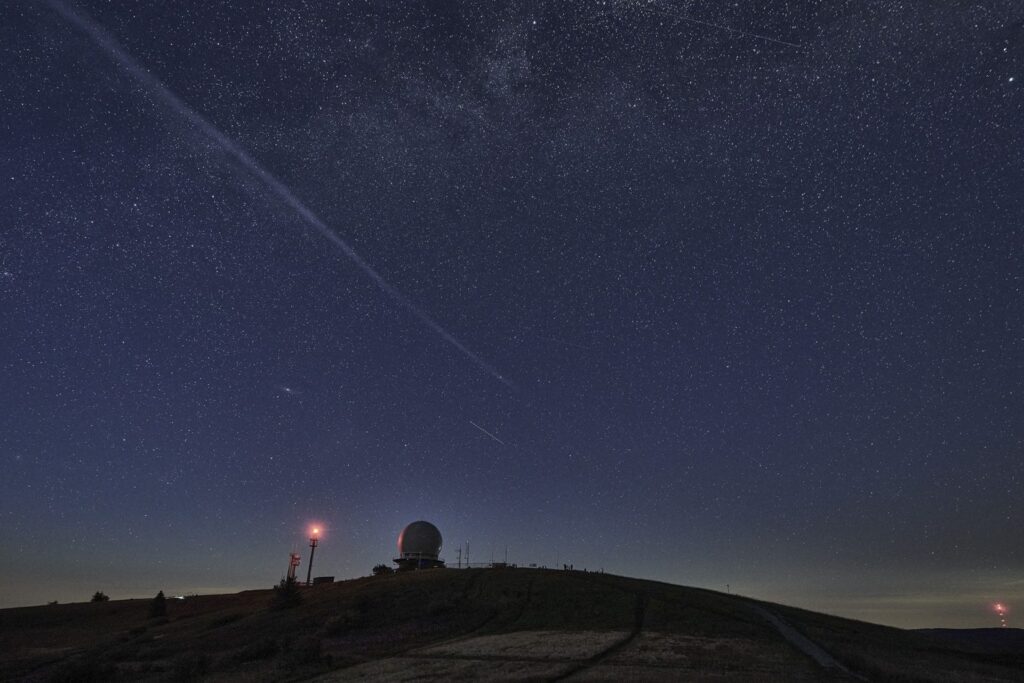 Sternenhimmel über der Wasserkuppe mit den Radarkuppeln am Horizont und der Spur eines Satelliten.