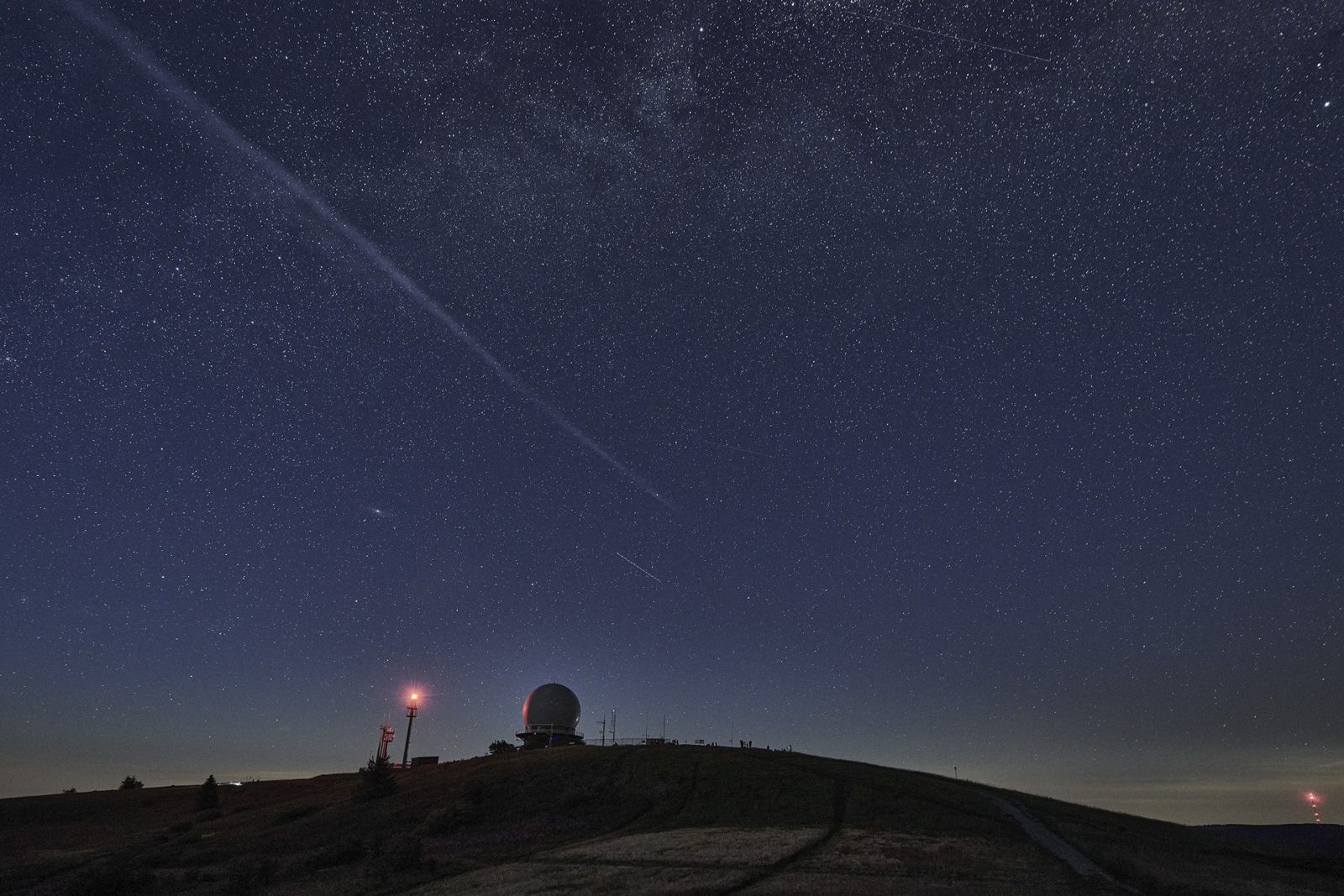 Sternenhimmel über der Wasserkuppe mit den Radarkuppeln am Horizont und der Spur eines Satelliten.