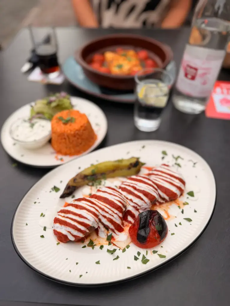 Beyti Soslu Köfte mit Bulgur und Cacık an einem Tisch draußen vor dem Tandurem in Fulda im Sommer